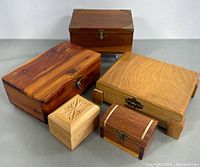 Five wooden jewellery and trinket boxes in various sizes arranged on a flat surface, variety of wood tones and finishes visible.