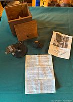 Overview photo showing all items included: the main tool grinder unit, additional component, instruction manual, and wooden storage box with sliding lid.