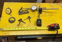 Top-down photo showing all seven assorted vintage metal tools arranged on a yellow surface with measuring tape for scale.