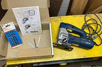 Bosch 1587VS jigsaw with extra cutters, manual, and original box on yellow surface.