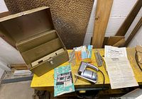 Full view of the sabre saw, metal toolbox, manual, edge guide, circle cutting attachment, and extra cutters laid out on a table.