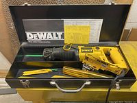 Dewalt reciprocating saw inside its metal carrying case with several blades and instruction manuals visible around it.