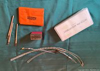 Contents of lot arranged on fabric: hitch pin assortment case, orange Allen wrench case, metal stamping set box, wire brushes