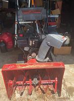 Front view of the red and black MTD snow blower showing the 26-inch auger housing with some wear and a partially disassembled front area exposing engine and belt housing.