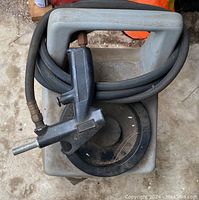 Top view of sandblaster gun and hose coiled on the tank lid with visible wear and some surface dirt on unit.
