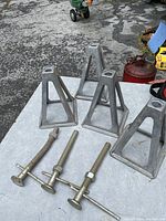 Four aluminum triangular jack stands displayed on a table with a background showing outdoor ground and other items.