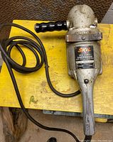 Full view of vintage Skil sander-grinder showing power cord, handle and tool body on yellow surface.