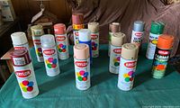 15 assorted spray paint cans from Krylon and Rust-Oleum in various colors including red, brown, beige, blue, green, orange scattered on a green cloth-covered table.