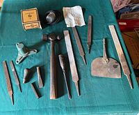 Top view of assorted vintage hand tools on green fabric including ball peen hammer, files, scraper tool, spray tool box.