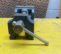 Front view of the vintage mini machinist vise showing the lever handle and body structure on a yellow surface.