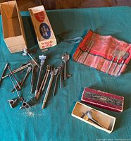 Overall view of assorted vintage wood drill bits including boxed Irwin bit, red roll-up pouch with bits, and loose bits on table