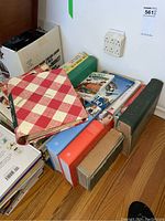 Books piled on floor showing various titles and bindings including a large green hardcover 'Birds of America' and red checkered cover book.