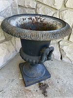 Front angled view of cast iron urn showing detailing on rim and handles, rust and wear visible