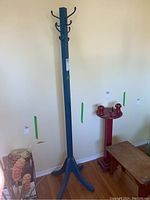 Photo showing the blue wooden coat rack against a plain wall with some adjacent furniture partially visible.