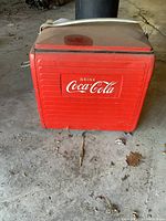 Front view of vintage red metal Coca Cola cooler showing embossed logo and overall condition.
