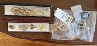 Wide shot showing collection of necklaces, pendants in boxes, a faux pearl necklace, several plastic bags containing pairs of cuff links, and a gold-tone butterfly brooch.