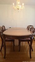 Front view of oval solid wood fruitwood dining table with curved legs and six chairs around it, chairs not included in lot.