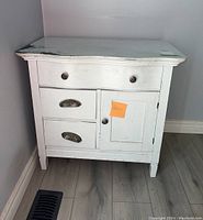 Front view of the vintage white wooden dresser showing two drawers and a cabinet door with metal knobs and handles, paint worn and chipped.