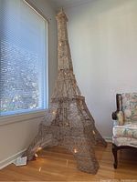 Full view of large gold-tone wire mesh Eiffel Tower light fixture by window with plug cord