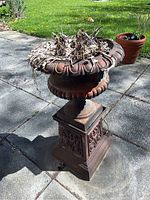 Full front view of urn and pedestal on patio, showing overall shape and surface patina.