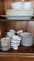 Shelved set of Johann Haviland tea cups, saucers and side plates with blue flowers and silver trim, stacked and organized for display.