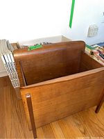 Wooden magazine rack from side angle, showing the overall shape and size related to the box of magazines behind it.
