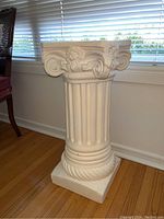 Front and side view of a white classical pedestal with fluted column shaft and ornate capital in floral and scroll motifs.