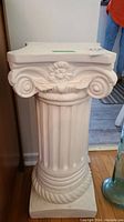 Front view of white ceramic Roman style plinth featuring fluted shaft and decorative capital with floral and scroll motif