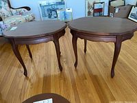 Pair of wooden oval side tables with cabriole legs on hardwood floor