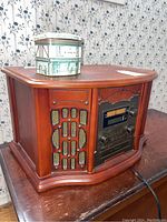 Front and side view of the vintage style stereo system showing the wooden cabinet, speaker grille and control panel with knobs and tuning display.