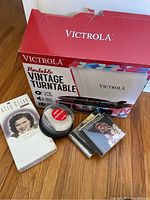 Victrola branded red and white box with portable vintage turntable visible, plus CDs and DVD discs with cover art including Kenny Rogers and Alison Clarke.