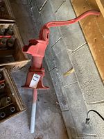 Full view of red cast iron manual well water pump lying on the ground in a garage setting next to wooden crates with bottles.