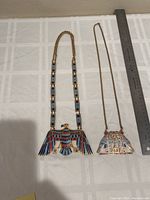 Two metal necklaces with Native American style designs and enamel inlays on white surface with ruler for scale.