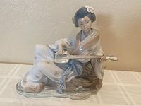 Front angled view of NAO by Lladro Geisha figurine playing shamisen with delicate detailing and color.