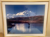 Front view of framed photographic print showing the full image and frame, depicting snow-capped mountains with a moose standing in the lake reflecting the landscape.