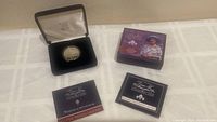 Photo showing the silver coin housed in a black presentation case, Certificate of Authenticity, and boxed packaging with Queen Elizabeth The Queen Mother image.
