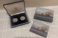Top view of two commemorative silver coins in black display case with original outer box and booklet on cloth surface
