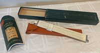 Slide rule with leather case, box, and manual displayed on table, showing overall lot components.