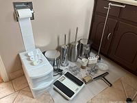 Full view of bathroom supplies including storage bins, toilet brushes, night lights, scale, metal canisters, and accessories.