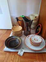 Overview of bowls, decorative plates, ceramic and wood items on floor.