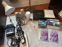 Overview of electronics and related items laid out on a white cloth, showing speakers, cassette player, GPS device, power bars, wiring, light bulbs, and language course materials