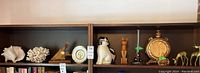 Two shelves with assorted decorative items including shells, clock, plate, cat figurines, brass candlestick and brass vase