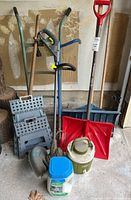 Full view of the entire garden tools lot showing trimmer, shovels, step stools, dolly, brush, jug, and ice melt container.