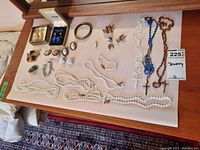 Full lot of jewelry displayed on beige paper including necklaces, rosaries, earrings, cufflinks, and brooches.