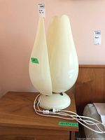 Front view of two off-white plastic table lamps with tulip-shaped shades on wooden surface.