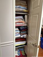 Shelves with a large quantity of folded assorted bedsheets and towels in various colors and fabrics.