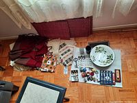 Wide photo showing folded fabric placemats, table cloths, various cutlery pieces, napkin rings, and ceramic bowl arranged on floor