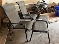Two metal frame outdoor chairs with gray fabric seating and backs paired with two matching stools with metal frames and fabric tops, located in a garage.