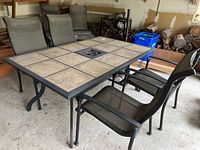 Image showing the outdoor metal and tile table with six large beige stone-pattern tiles, surrounded by four mesh chairs.