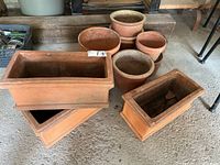 Overall view of three rectangular terra cotta planters and a stack of round pots and bases, showing the assortment in weathered condition.